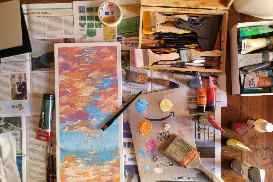 絵の具や筆、描きかけの絵が並ぶ制作机を上から見た様子